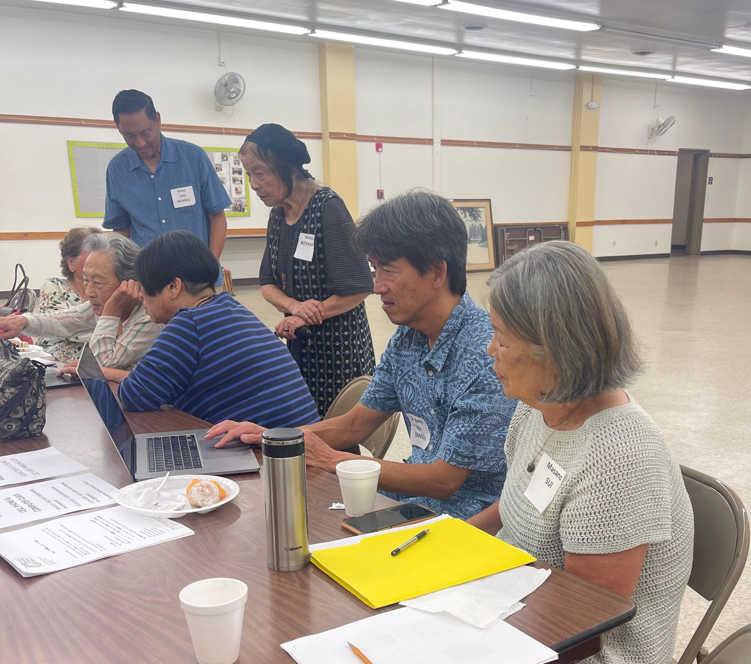 Barry Goy assisting seniors with their cell phones & computers at Seinan-Koreisha's Kashu club